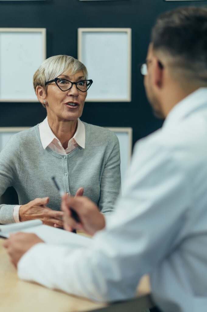 Smiling senior woman patient in doctor's office counseling a male doctor